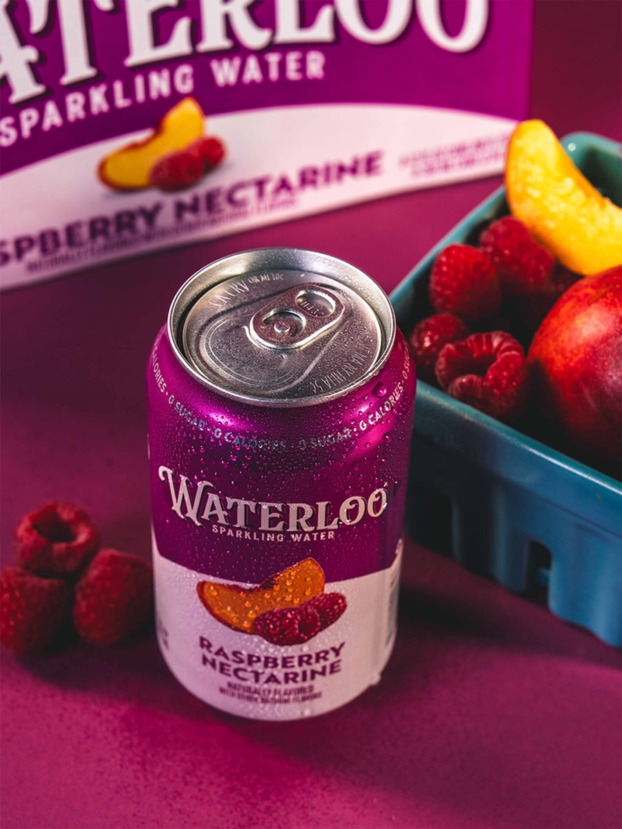 Waterloo Raspberry Nectarine sparkling water can with fresh raspberries and peaches in the background.