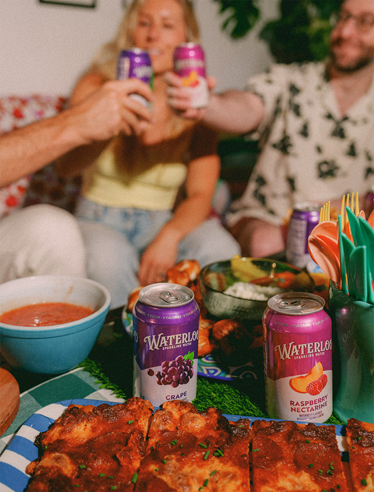 Friends toasting with Waterloo sparkling water cans at a festive meal with delicious food.