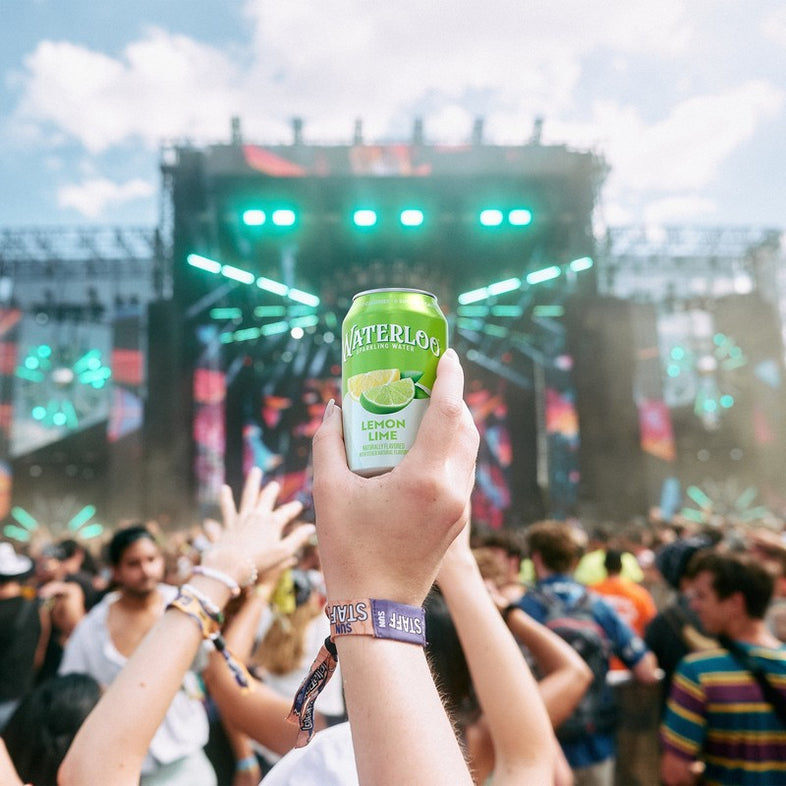 A hand holding a can of Waterloo Lemon Lime sparkling water at a lively outdoor concert.