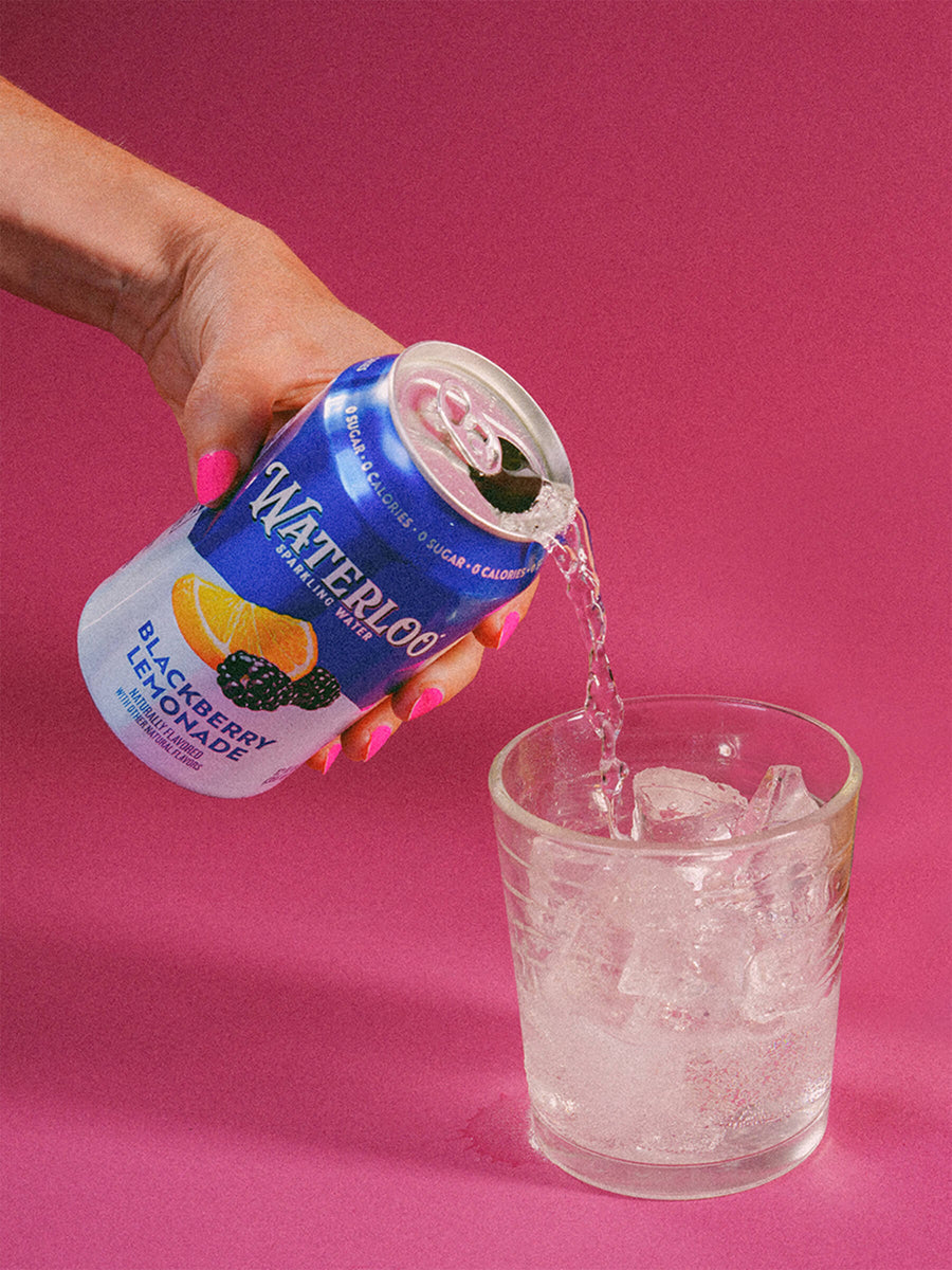 Person pouring Waterloo Blackberry Lemonade sparkling water into a glass with ice, set against a vibrant pink background.