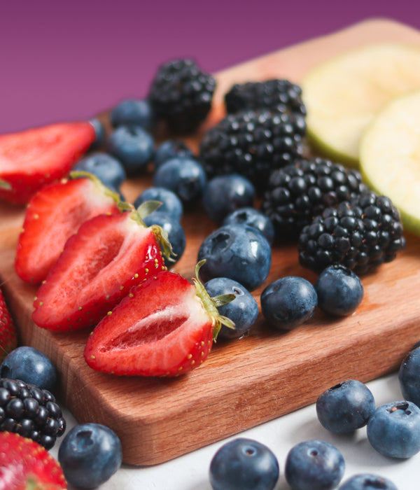 Vibrant assortment of fresh strawberries, blueberries, blackberries, and apple slices on a wooden cutting board.