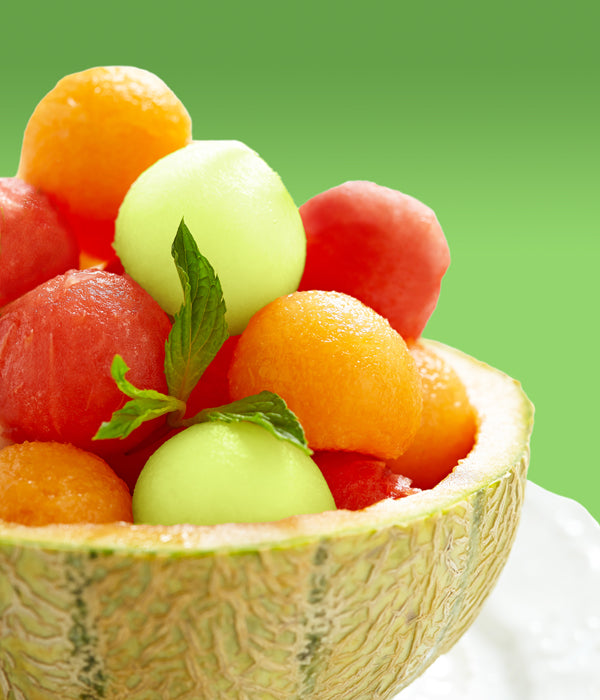 Colorful fruit salad with melon balls and mint in a halved cantaloupe, set against a green background.