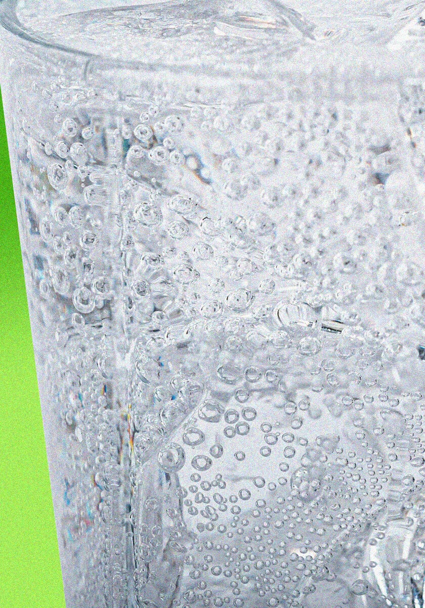 Close-up of a glass filled with sparkling water, showcasing bubbles and clear ice cubes with a vibrant green background.