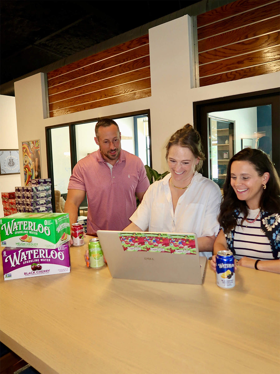 Three people engaged in a discussion with Waterloo sparkling water cans and a laptop on a wooden table.