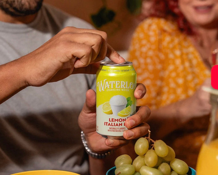 Person opening a can of Waterloo Lemon Italian sparkling water, surrounded by fresh grapes.