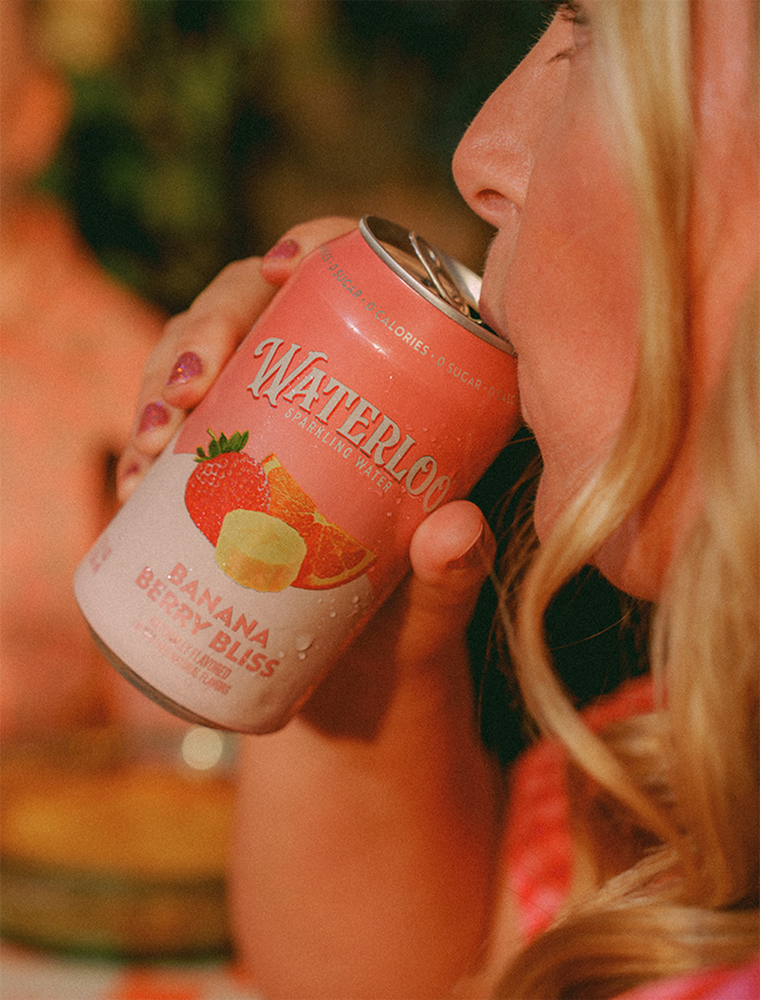 A close-up of a person sipping Waterloo Banana Berry Bliss sparkling water from a can, showcasing its vibrant packaging.