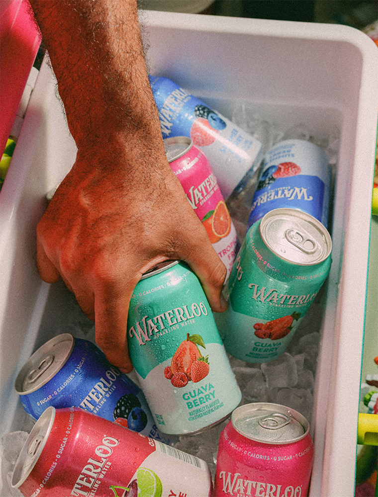 Hand reaching for colorful Waterloo sparkling water cans in a cooler filled with ice.