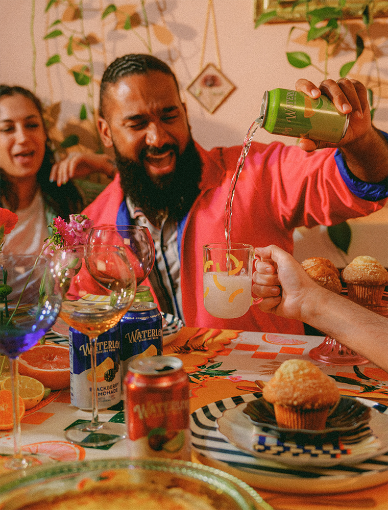 A joyful gathering with friends, pouring a drink into a mug, surrounded by colorful food and beverages on a vibrant table.