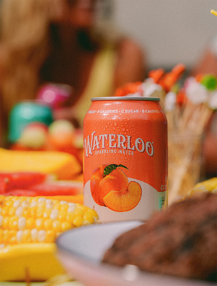 Can of Waterloo sparkling water with a peach flavor, surrounded by fresh fruits and vibrant colors.