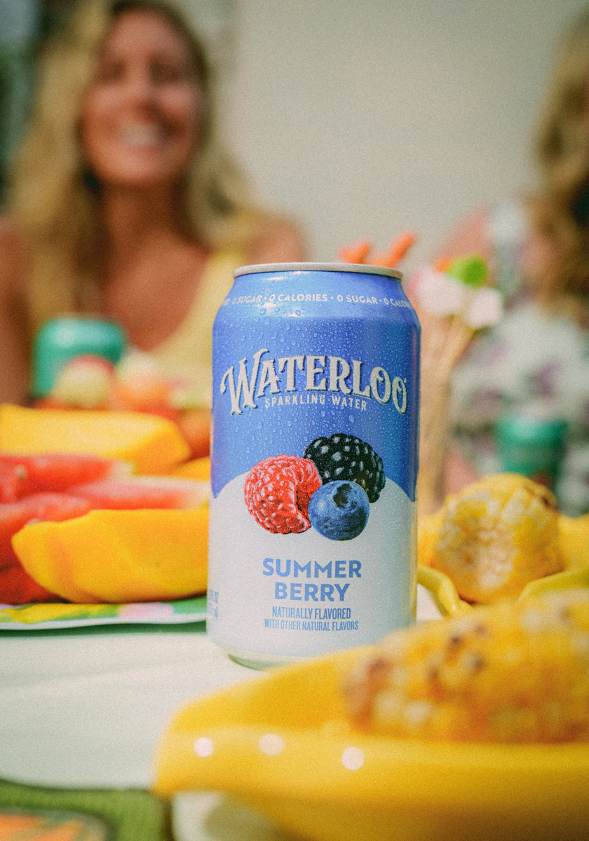 Can of Waterloo Summer Berry sparkling water surrounded by colorful summer fruits at a lively gathering.