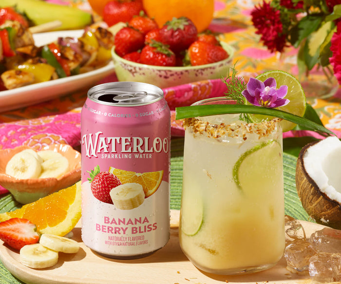 A refreshing glass of Banana Berry Bliss sparkling water with fruit and flowers on a colorful table setting.