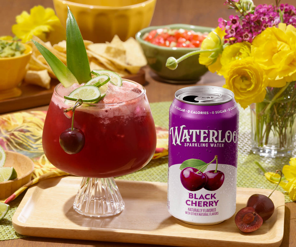 Refreshing Black Cherry Waterloo sparkling water next to a vibrant fruit cocktail garnished with cherries and lime.