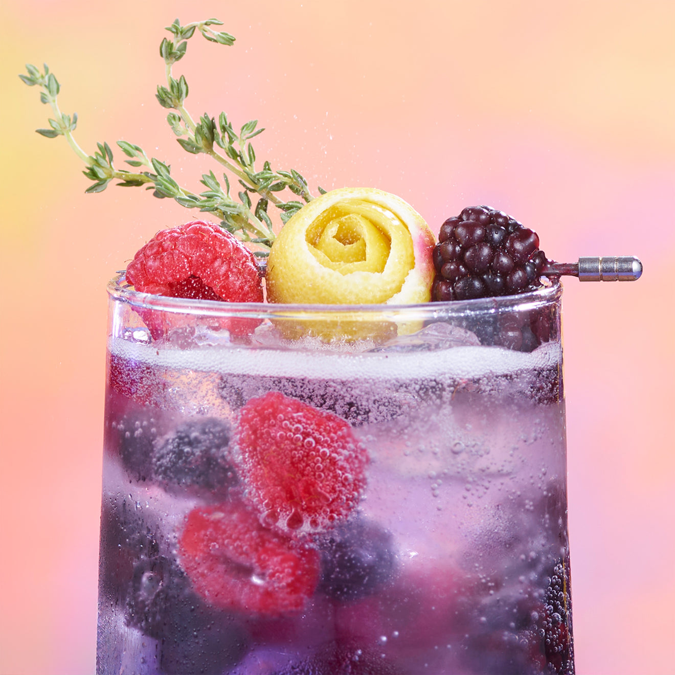 Refreshing cocktail with raspberries, blackberries, and lemon garnish, set against a colorful blurred background.