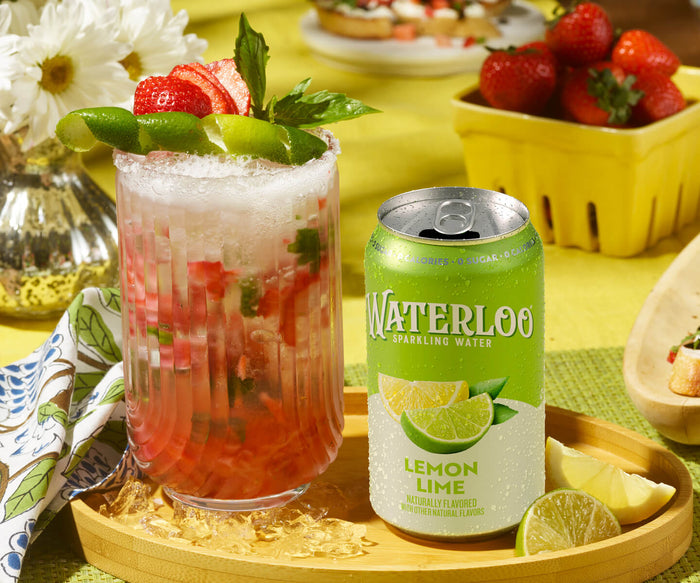 Refreshing lemonade mocktail with strawberries and lime beside Waterloo Lemon Lime sparkling water can.