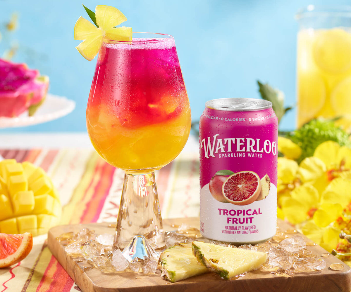 Colorful tropical drink topped with ice and a lemon slice, with Waterloo Tropical Fruit sparkling water can beside it.