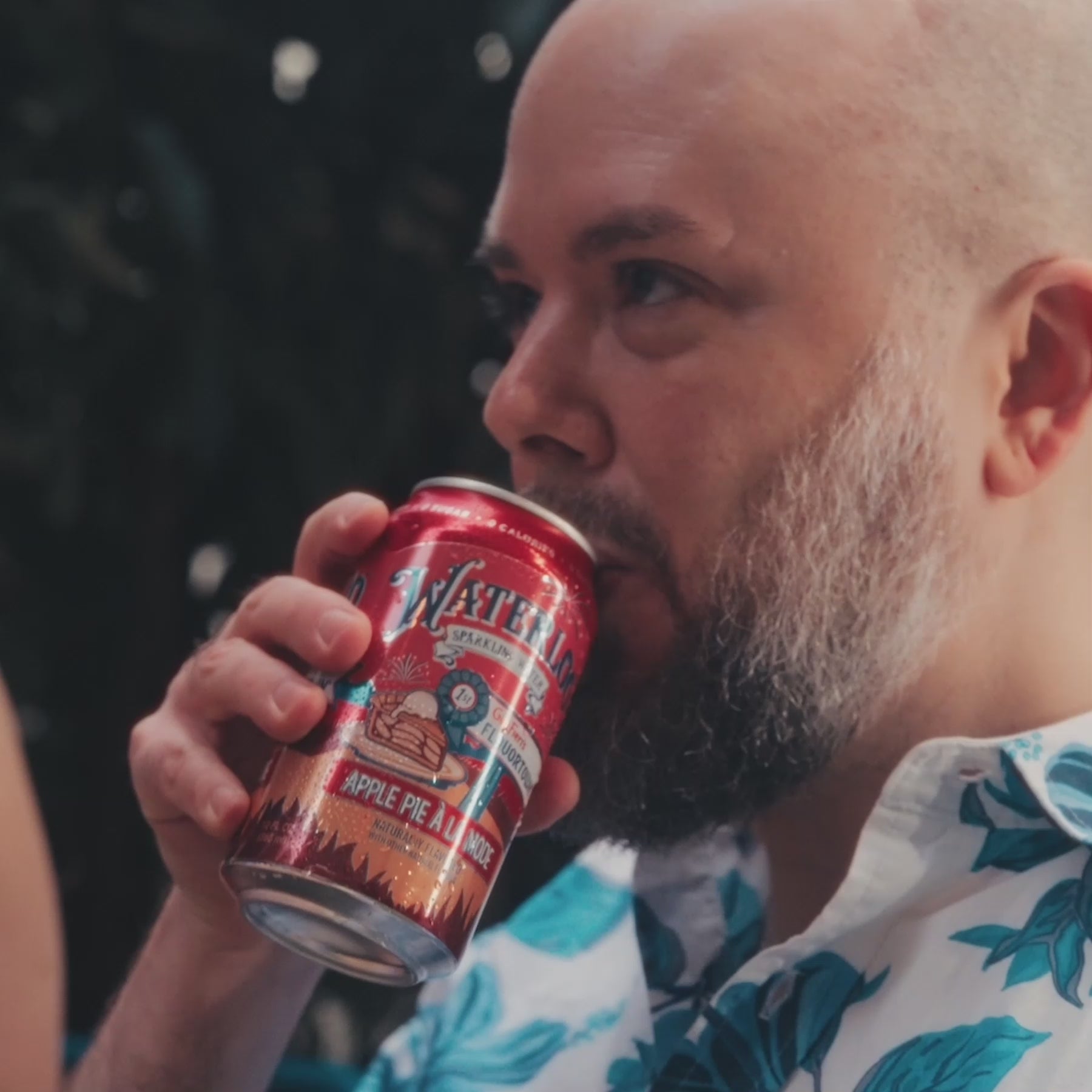 A man enjoying a can of sparkling water labeled 'Apple Pie à la Mode' in a tropical shirt.