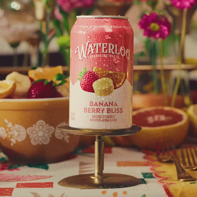 A can of Waterloo Banana Berry Bliss sparkling water surrounded by fruits on a colorful table setting.